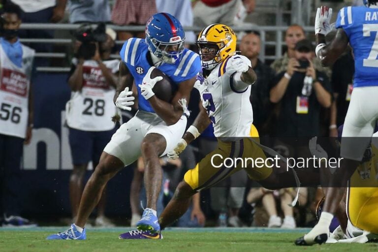 An Ole Miss player carries the football while an LSU defender tries to tackle him during a college game.