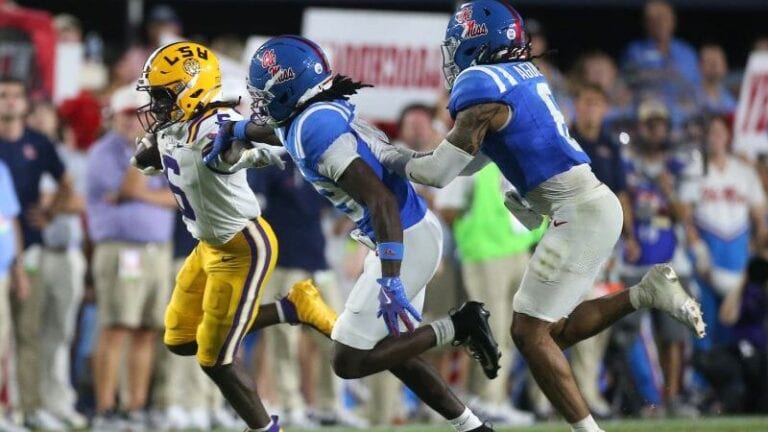 An LSU player runs with the football while two Ole Miss defenders try to tackle him during a game.