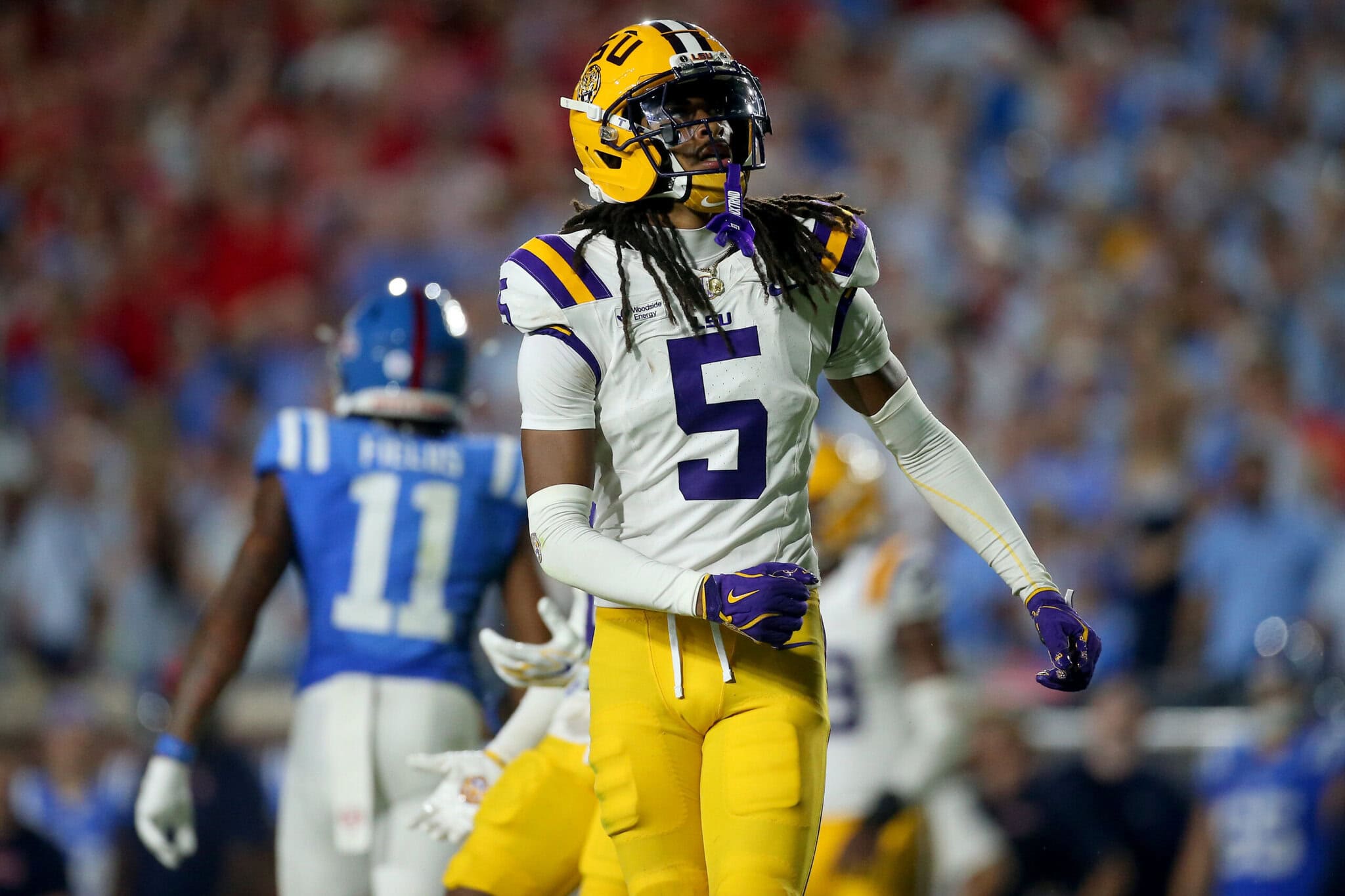 An LSU football player in a white and yellow number five jersey stands on the field during a game against Kentucky.