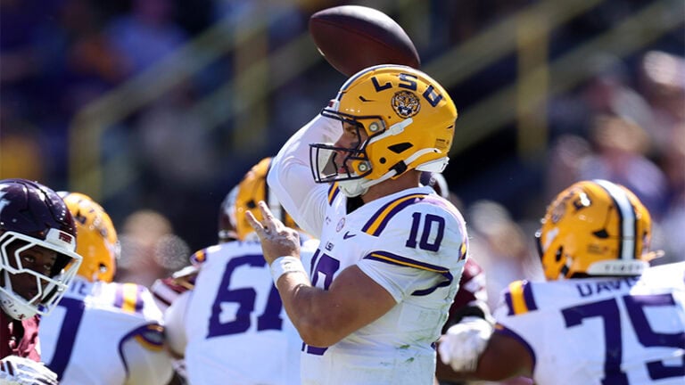 An LSU quarterback in a white jersey prepares to throw a football during a game.