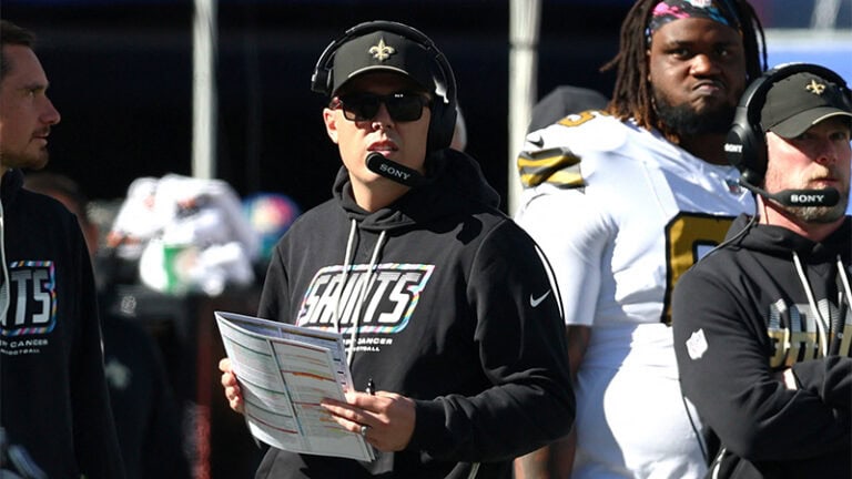 A New Orleans Saints coach on the sideline, wearing a headset and holding a Steelers play sheet.