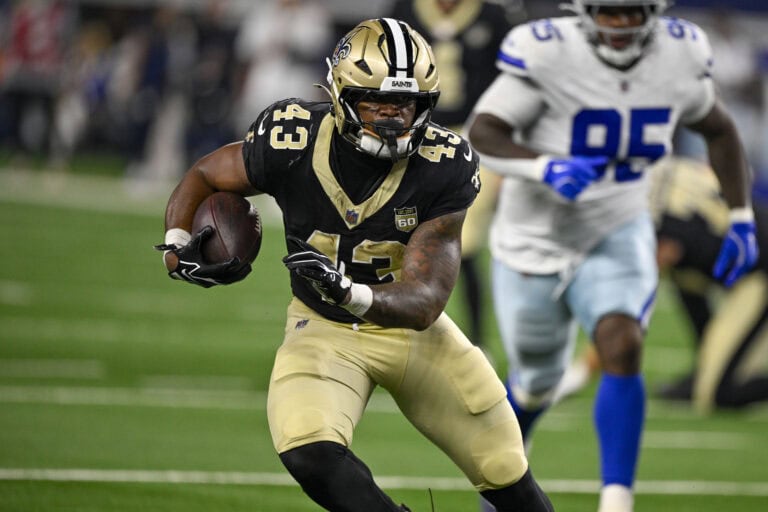 A Saints player in a black uniform runs with the ball as a Giants defender pursues him.