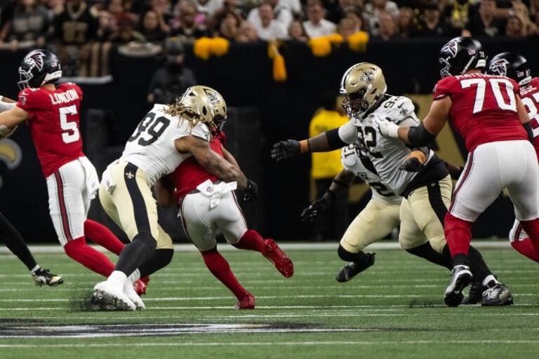 New Orleans Saints players in white uniforms tackle an Atlanta Falcons player in red during an NFL game.