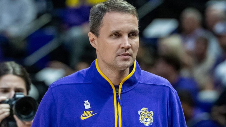LSU basketball coach Matt McMahon stands on the court wearing a purple team jacket.