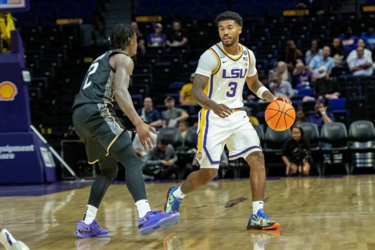 An LSU men’s basketball player dribbles the ball while guarded by an opponent in a dark jersey.