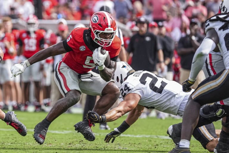 A Georgia player in a red jersey runs with the ball as a Vanderbilt defender tackles him during the Week 6 game.