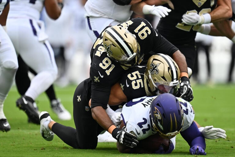 Two New Orleans Saints players tackle a Baltimore Ravens player on the field.