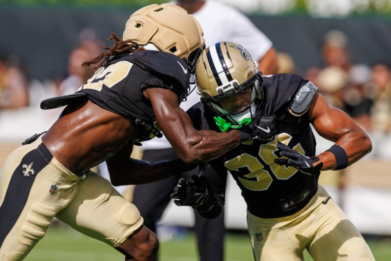 Two New Orleans Saints players in black and gold uniforms participate in an NFL practice drill.