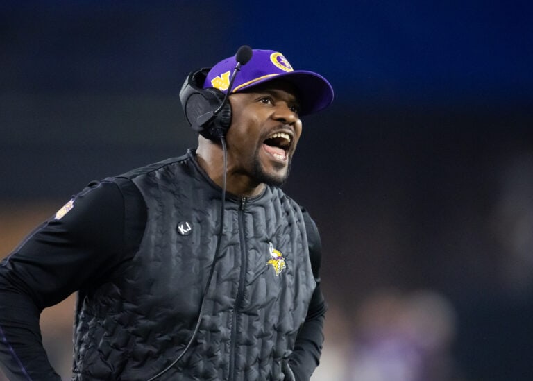 Minnesota Vikings coach Kevin O’Connell shouts instructions to his offense from the sidelines wearing a headset and cap.