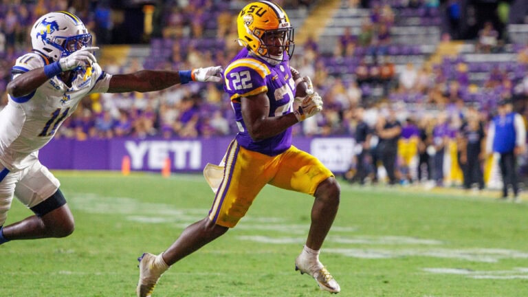 An LSU football player runs with the ball as a Kentucky player chases him.