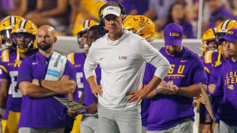 LSU coach Brian Kelly stands on the sidelines with players and staff in purple and gold gear during the McNeese game.
