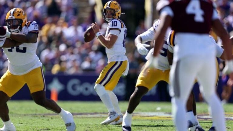 An LSU quarterback prepares to throw a pass while surrounded by teammates and opponents on the field.